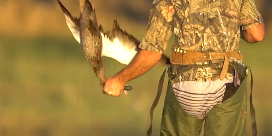 A duck shooter holding a duck by the neck