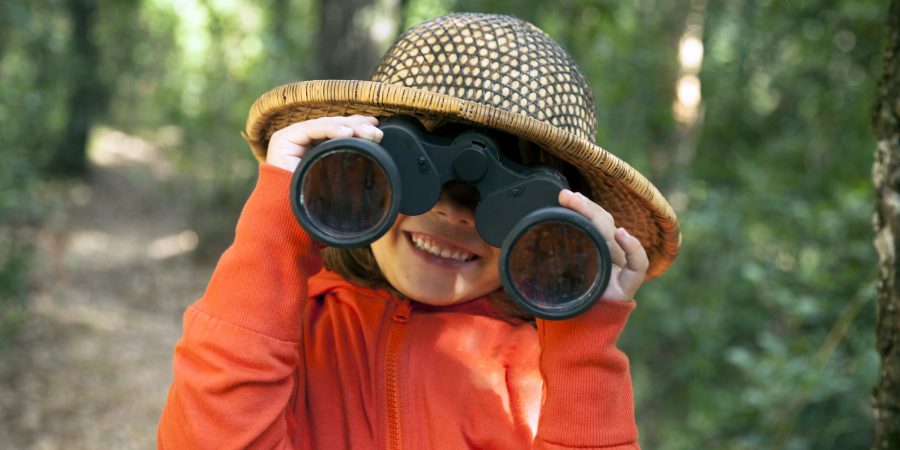 A young girl looks playfully through binoculars at the camera.