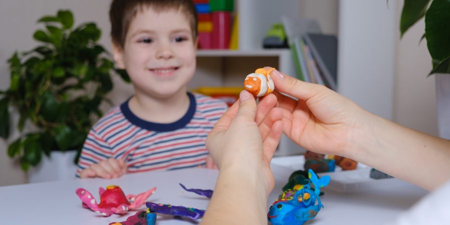 A child with a big smile looks at a plasticine model of a clown fish.