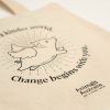 Natural cotton tote bag with an outline image of a flying pig, black AA logo, and the words 'Imagine a kinder world. Change begins with you.'