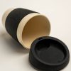 Beige reusable coffee cup with black band and lid. Band embossed with the AA logo Lid is off and sitting in front of the mouth of the cup