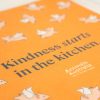 Angled view of tea towel with the words "kindness starts in the kitchen" and images of illustrated flying pig