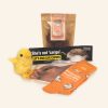 A group of products including a plush chick, live export bumper sticker, cow tea-towel, orange socks and a pack of chocolates.