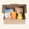 A gift pack in a cardboard box with a plush chick, cow tea-towel, orange socks, a pack of chocolates and a live export bumper sticker.