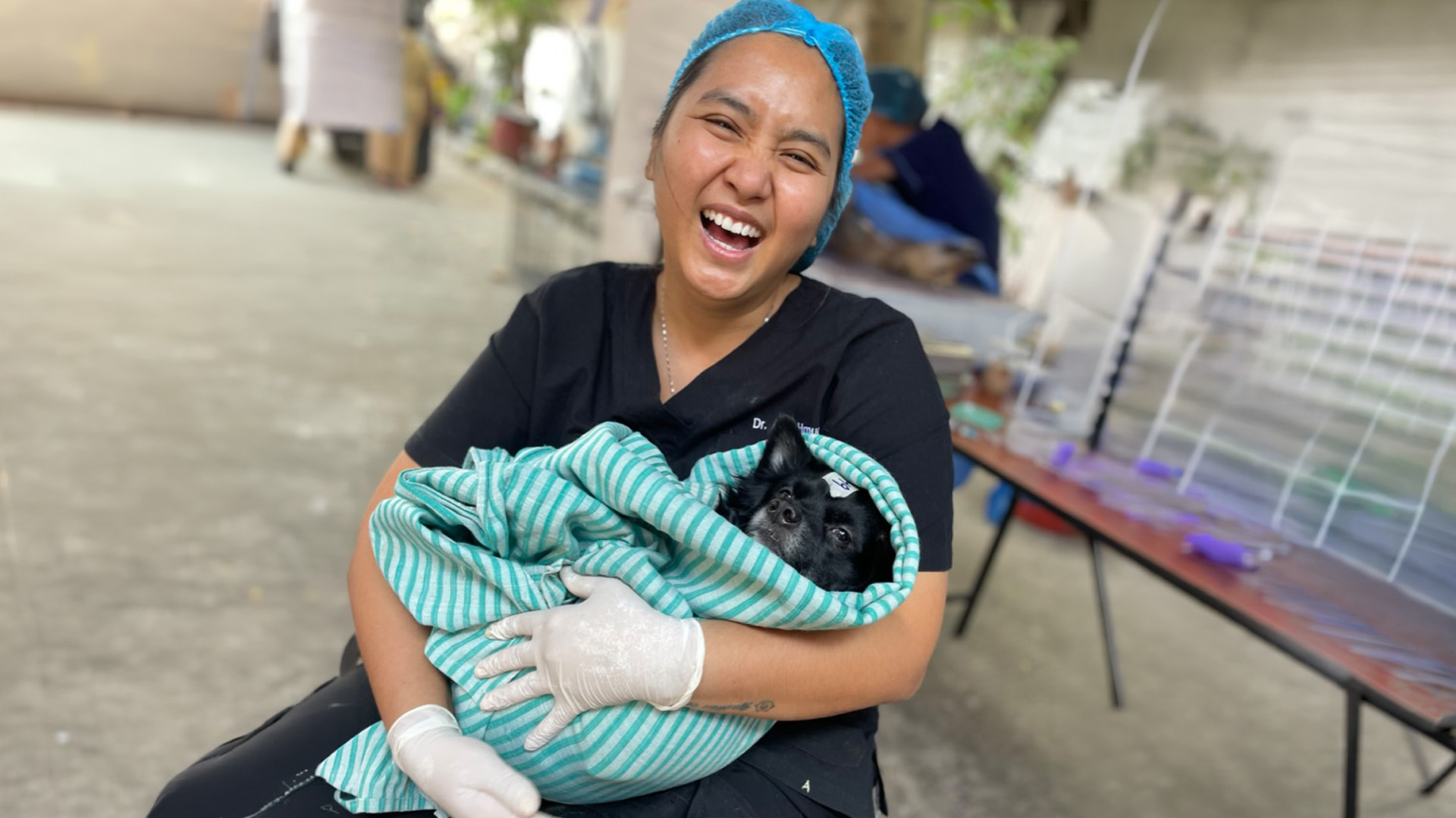 A smiling woman holds a dog in a blanket in an animal shelter setting.
