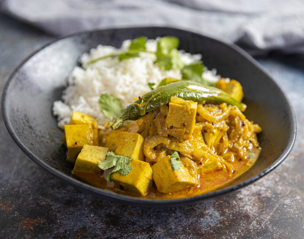 Delicious looking tofu masala curry with rice on side in a bowl
