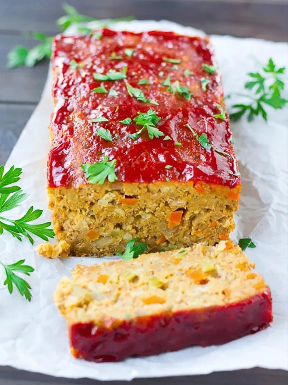 A plant-based meatloaf log sits on baking paper. It is garnished with parsley, and a slice is cut revealing the centre.