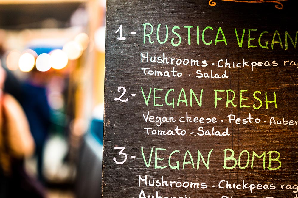 A handwritten menu board out on the street, showing three vegan menu options.