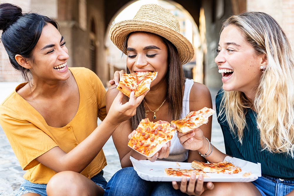 Three friends sit outside sharing a vegan pizza. 