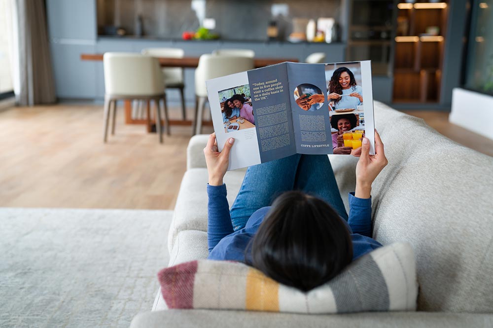 A woman lays back on the couch, reading a magazine.