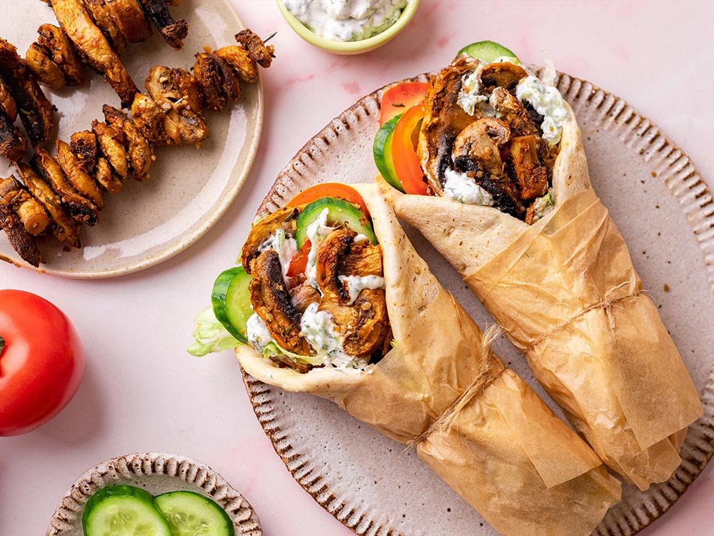 Overhead view of two mushroom shawarmas on a plate, surrounded with extra mushroom, tomato, cucumber, and tzatziki.