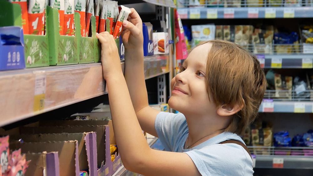 A young boy us grabbing a treat from the confectionery aisle and smiling happily.