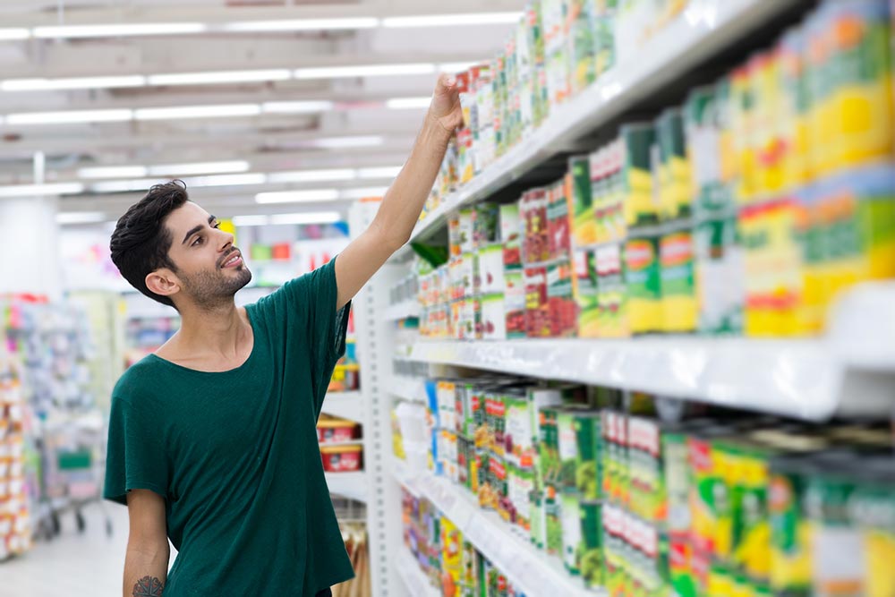 A man grabs a tin from the canned goods section of the supermarket.