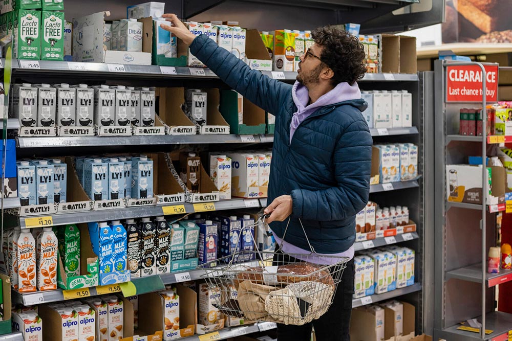 A man reaches for a shelf stable plant-based milk in the supermarket aisle.