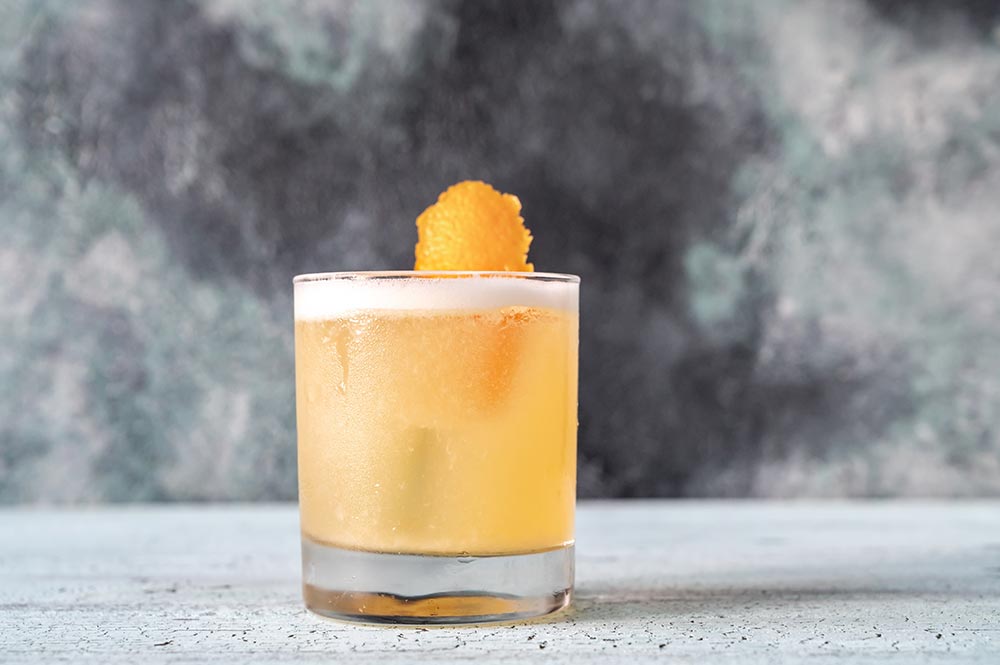 A frontal view of a whisky sour made with aquafaba, in a short tumbler, decorated with orange rind.