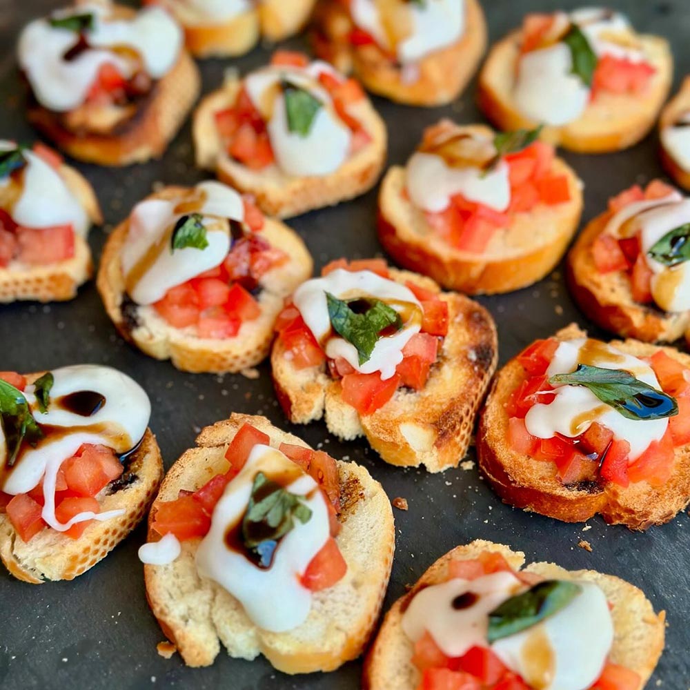 A tray of bruschetta topped with tomato, balsamic, and Imber's Pantry plant-based mozzarella.