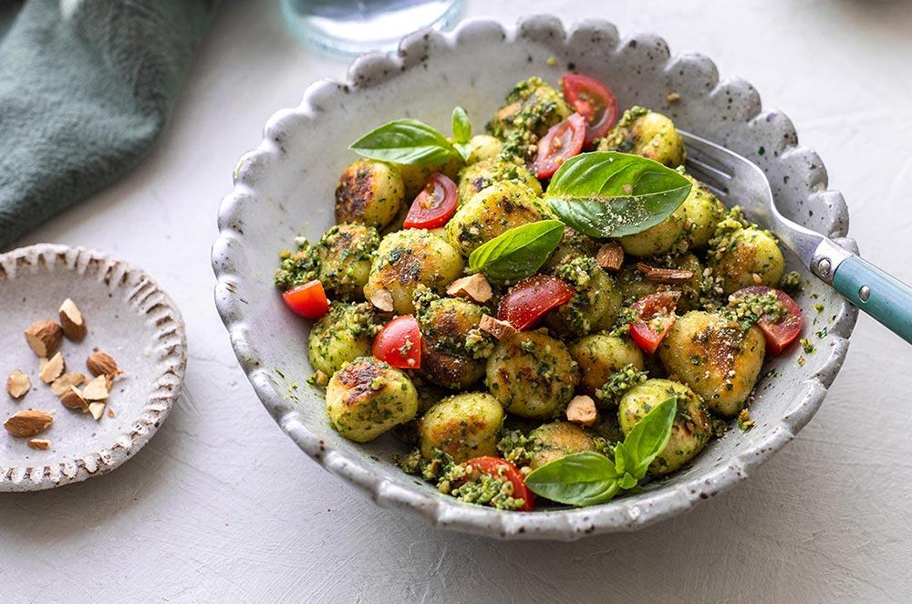 A bowl of pan-fried gnocchi slathered in pesto garnished with basil leaves.