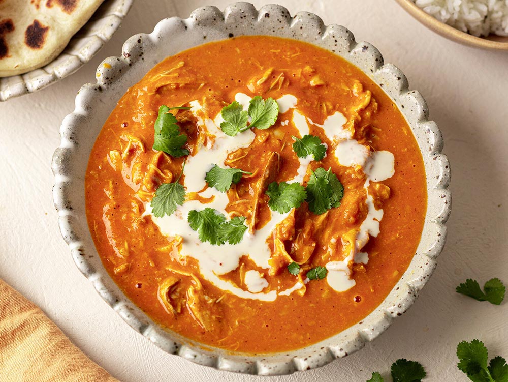 A bowl of butter 'chicken'. The chicken is made from banana blossom. It's topped with a plant-based cream and garnished with greens.