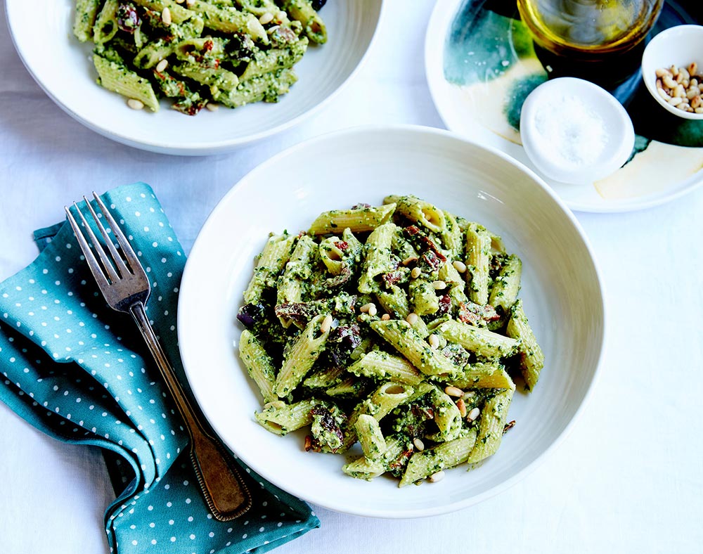 And overhead view of two bowls of penne pasta smothered in green pesto.