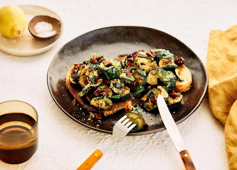 Two slices of sourdough with grilled and smashed zucchini and almonds.