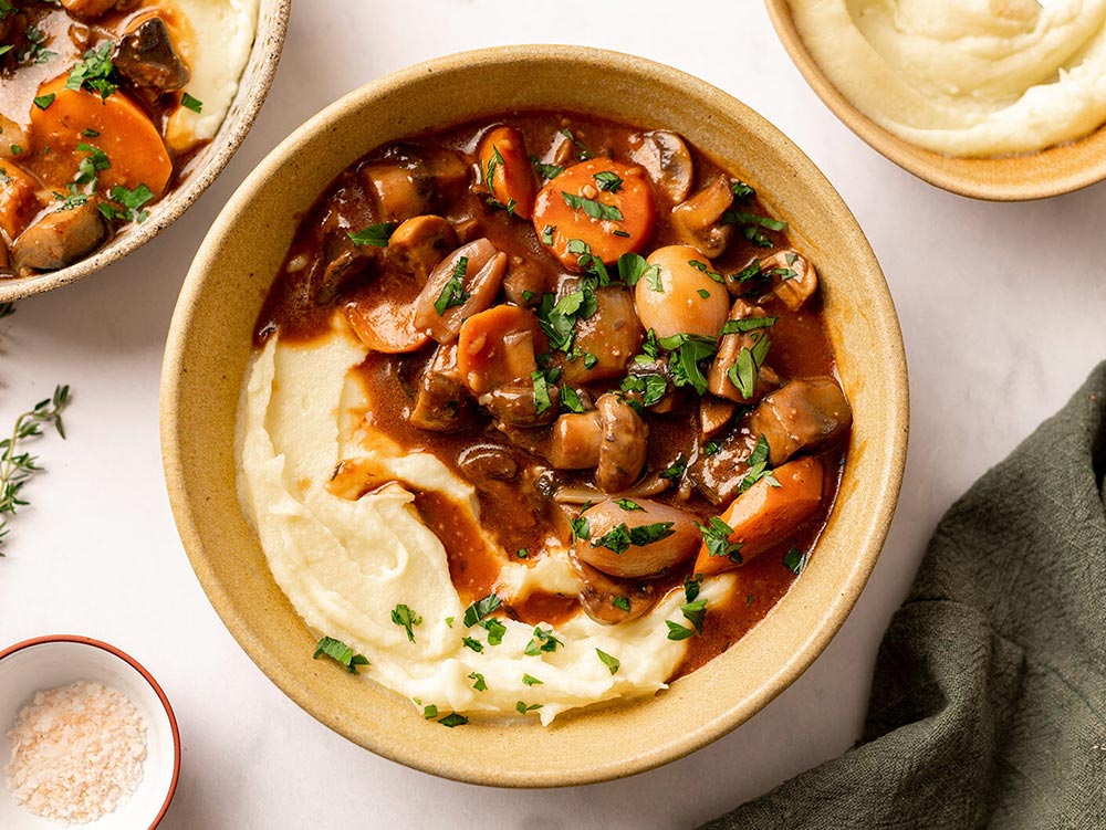 A bowl of gravy-laden mushroom bourguignon with a side of creamy mashed potato. 