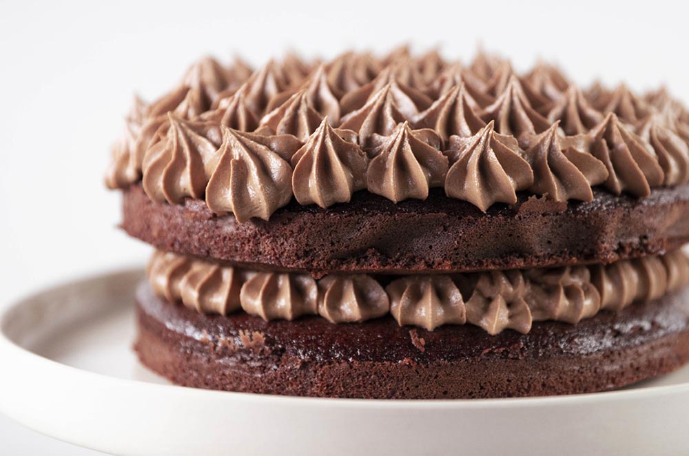 A close up of a beautifully decorated and piped two tiered chocolate cake. 