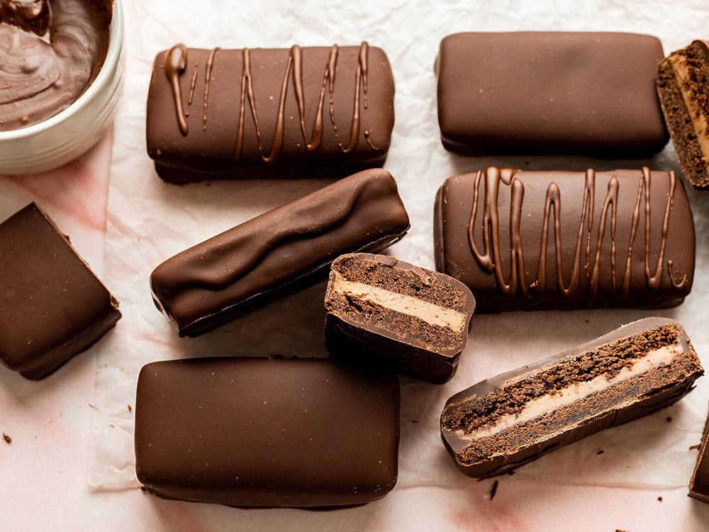 An overhead view of homemade tim tams. A couple of them are sliced in half to reveal the soft cross section. 