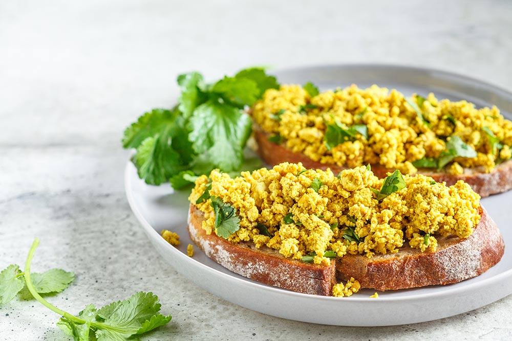 A plate with tofu scramble served over two slices of toast, garnished with herbs.