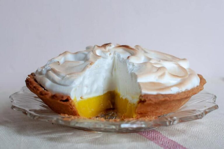 A front on view of a lemon meringue pie with a slice taken out, revealing the cross section. The meringue is light and fluffy, and has been torched beautifully.