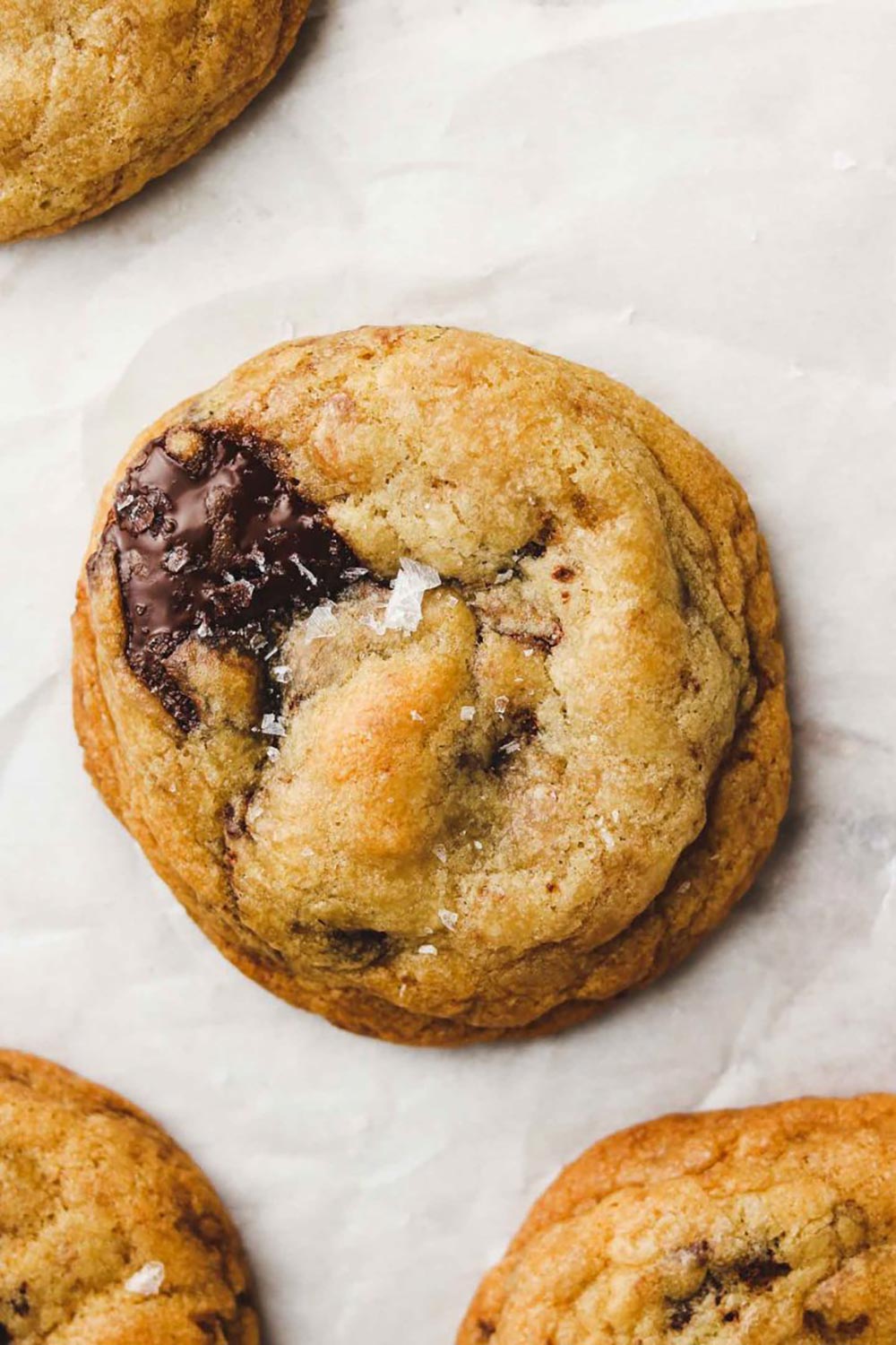 An overhead close up of a choc chip cookie. The chocolate is still melted as though it's fresh out of the oven. It has a sprinkle of sea salt. 