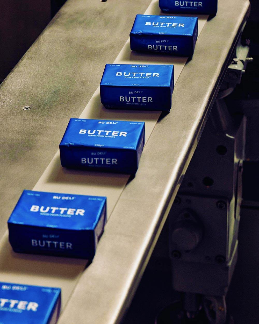 A conveyor belt of Bu Deli vegan block butters in their royal blue packaging.