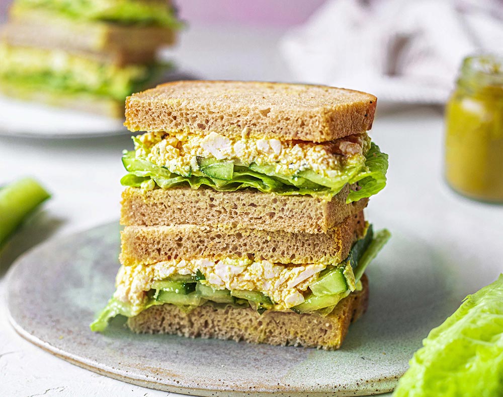 Two halves of a vegan egg and lettuce sandwich face the camera, to show the fillings.