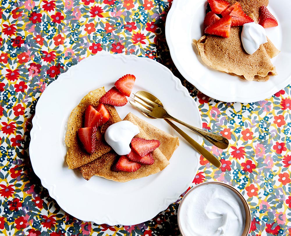 Beautifully presented crepes decorated with cream and strawberries on a plate. 