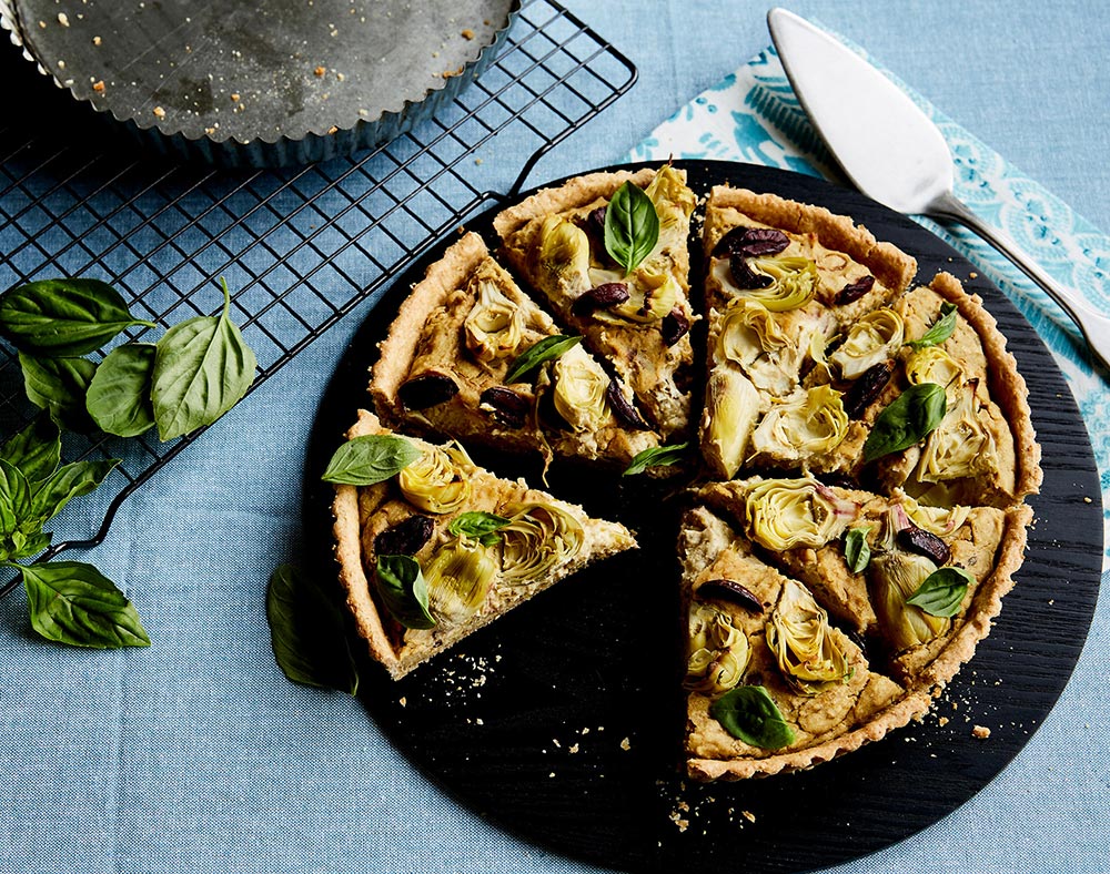 A beautifully presented artichoke and olive quiche in a shortcrust pastry crust. It has been cut into slices, with one slice missing. 