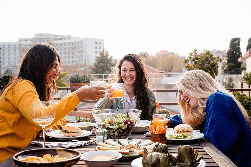 Three friends sharing a healthy vegan meal outdoors on a rooftop.