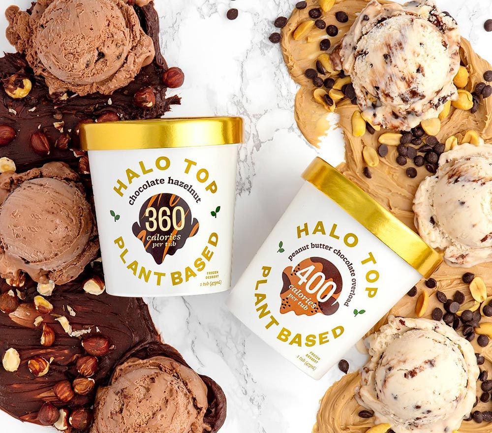 Two tubs of different Halo Top ice cream flavours are lying on a marble bench, surrounded by scoops of ice cream, some choc hazelnut, some peanut butter choc chip.