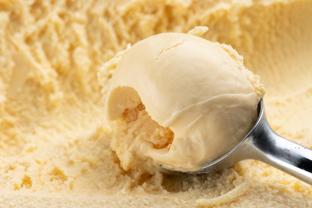 A vanilla ice cream being scooped up from a tub. 