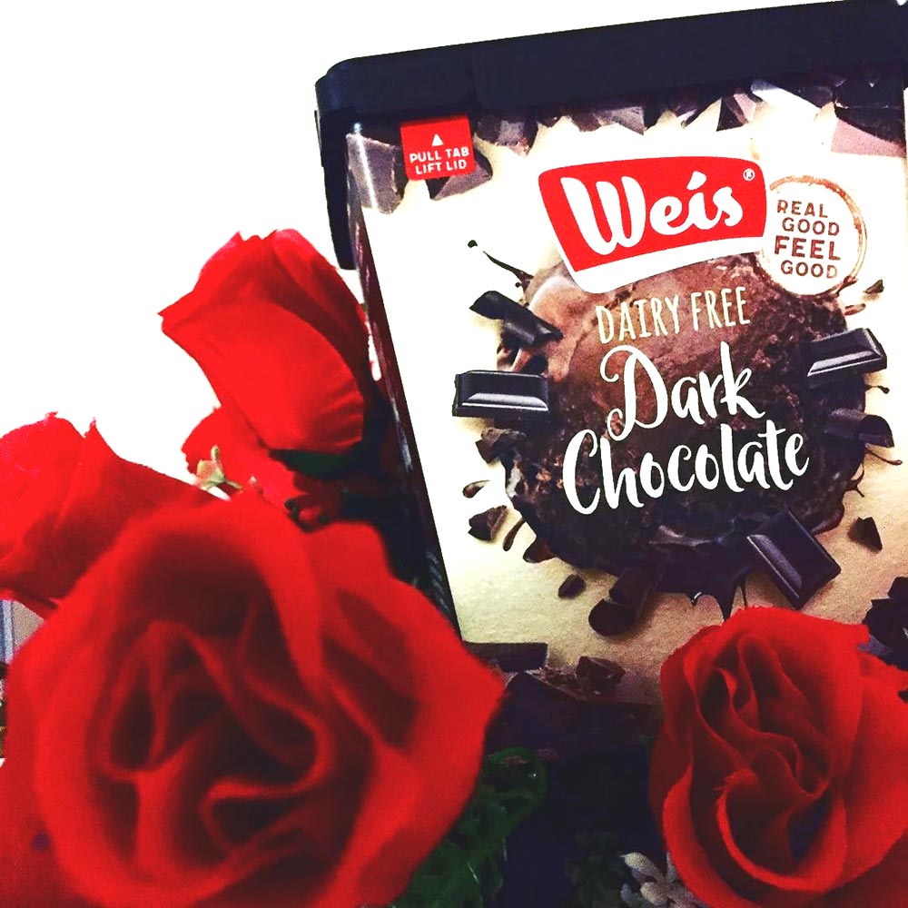 A tub of dairy-free dark chocolate Weis ice cream sits atop red roses.