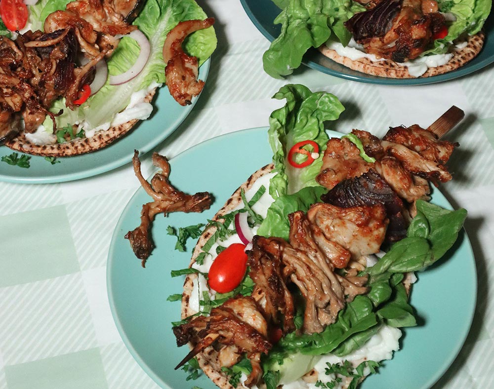 Plant-based 'lamb' shish kebabs on served on green plates at a table setting.