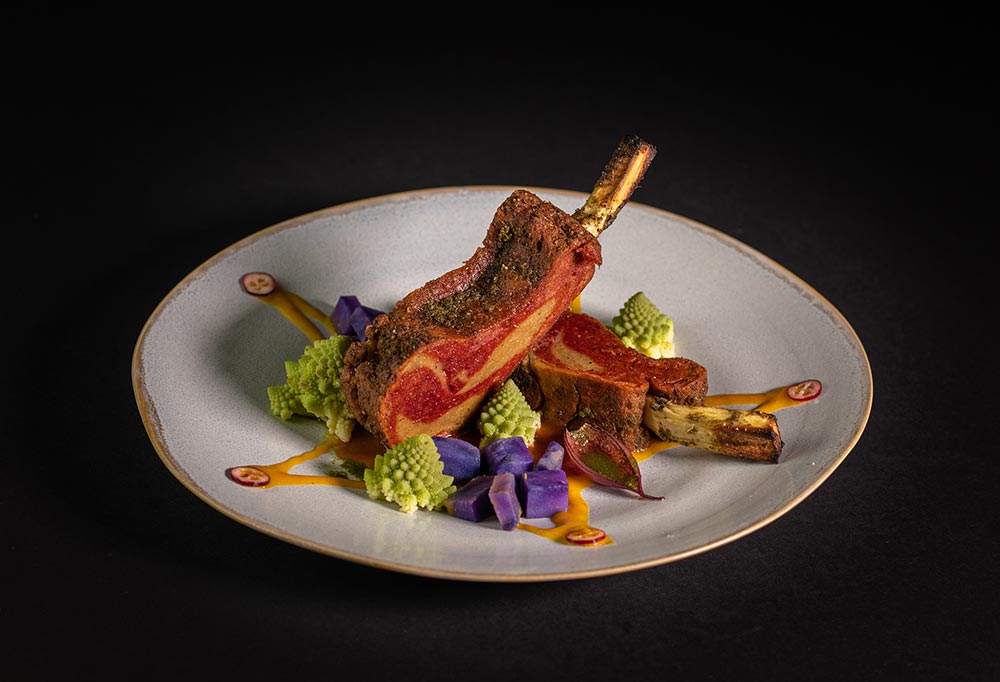 A rack of seitan 'lamb' is beautifully presented on a white plate. 