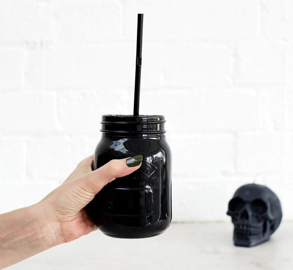 A hand holds a jet black glass up in front of a white brick background.