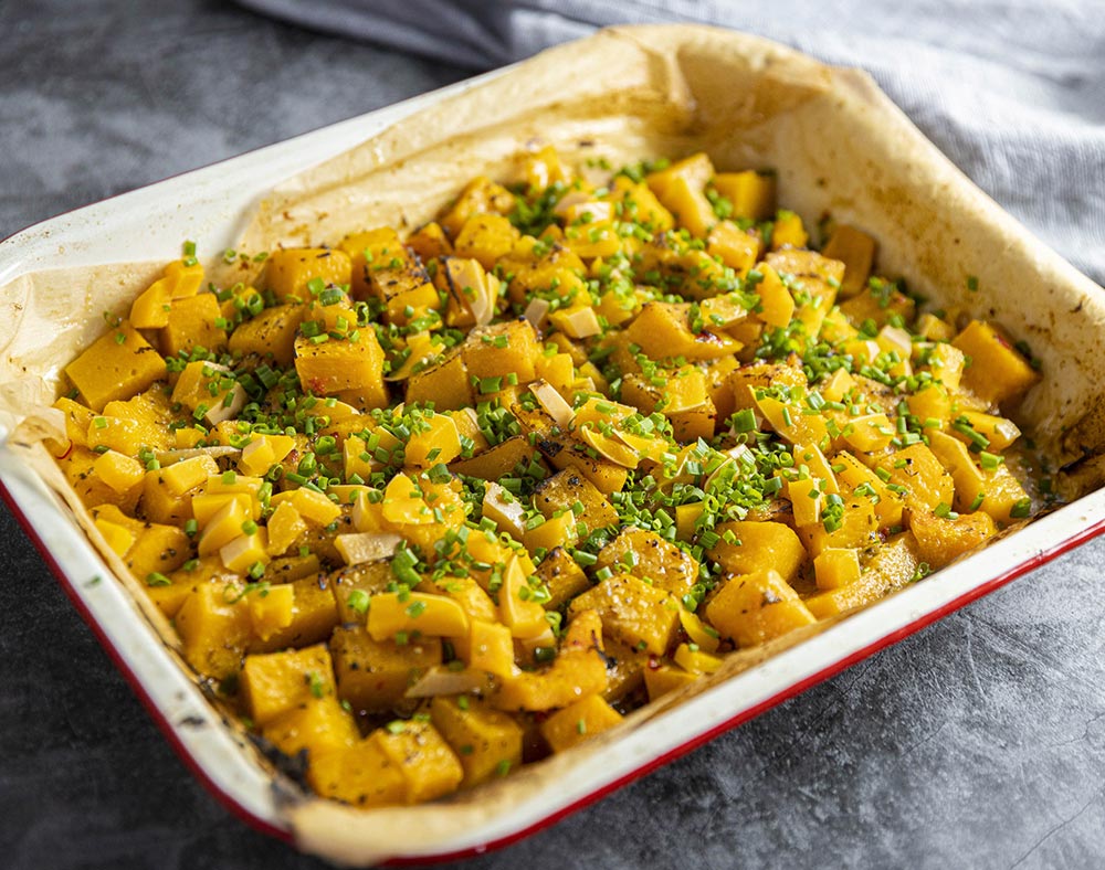 A tray of roasted pumpkin cubes with a herb garnish.