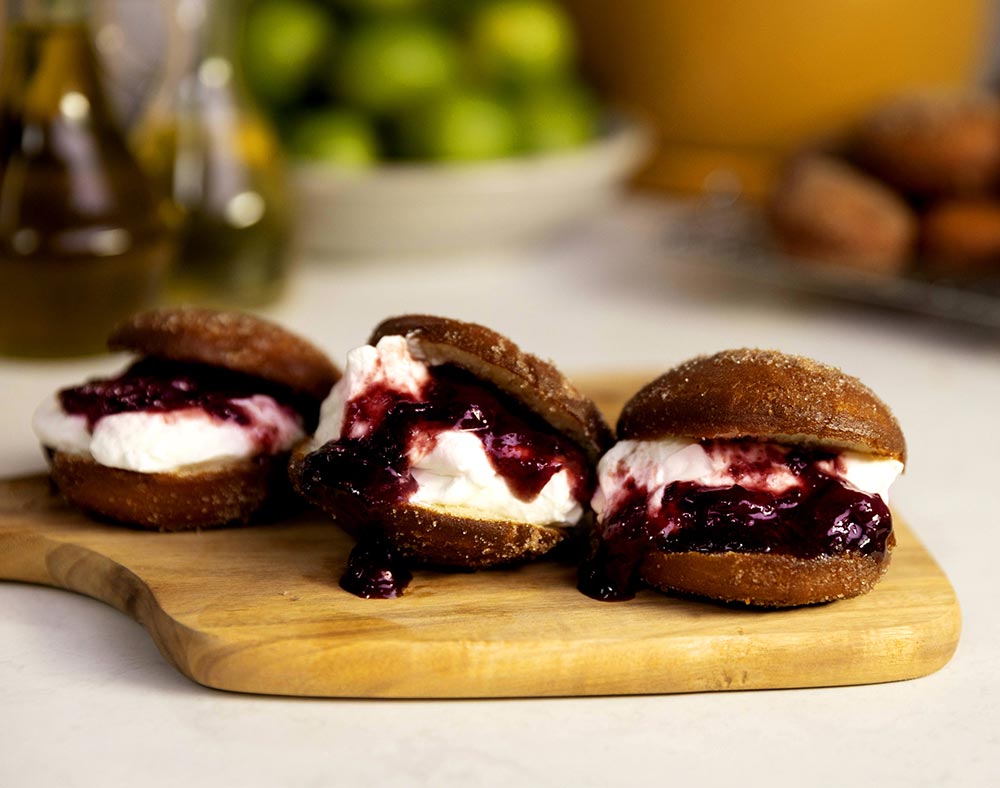 Three mini jam and cream-filled doughnuts sit on a small wooden serving board.