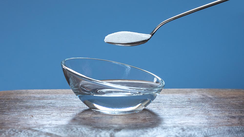 A small clear bowl of vinegar with a spoon full of bicarb soda above ready to pour in.