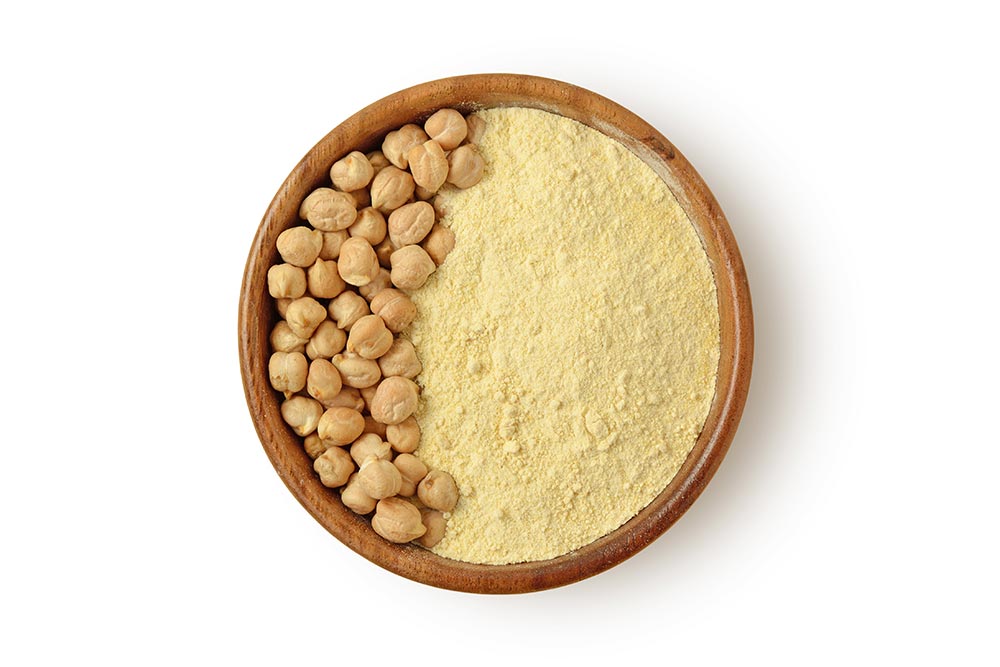 A bowl of chickpea flour, with full chickpeas to one side.