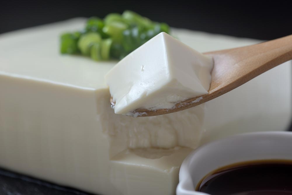 A wooden spoon breaking into a block of silken tofu.