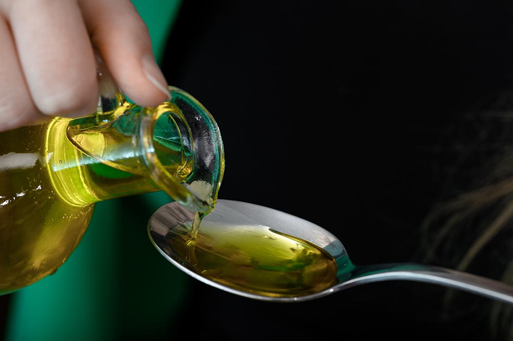 A hand pours vegetable oil onto a tablespoon.