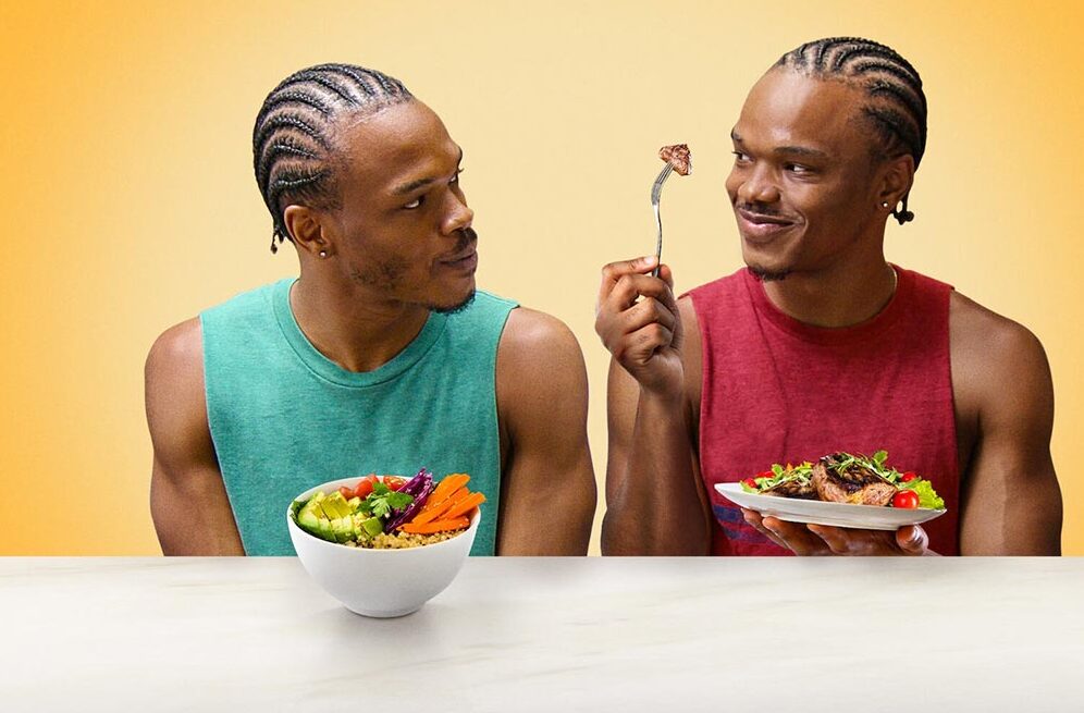 A pair of twins looking at each other while eating.