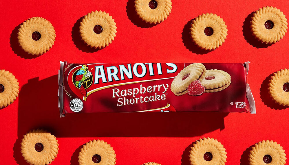 A packet of raspberry shortcakes sit on a red background, with biscuits scattered all around.