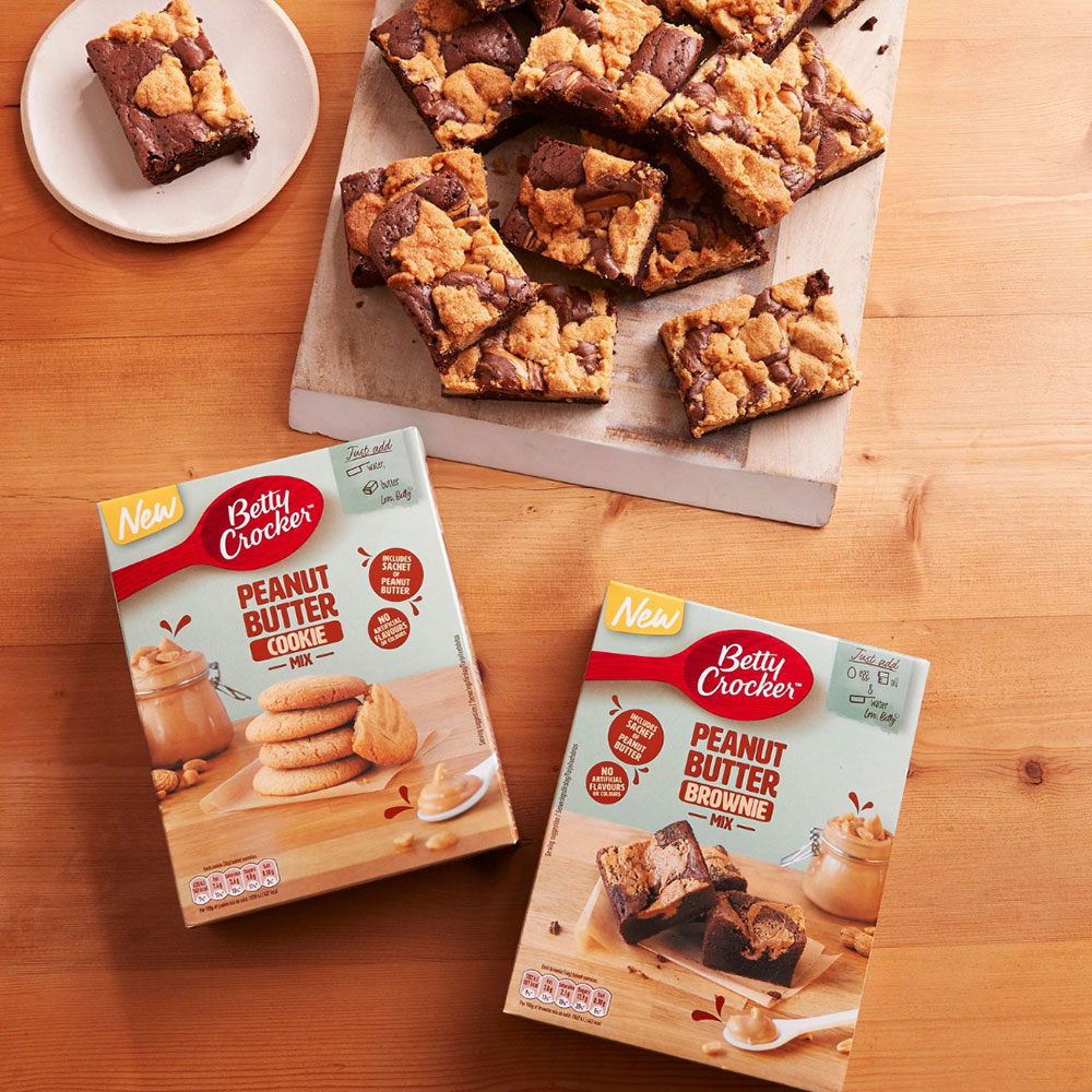 A tray of peanut butter brownies sit on a bench, with a two boxes of Betty Crocker mixes both nearby - peanut butter cookie mix and peanut butter brownie mix.